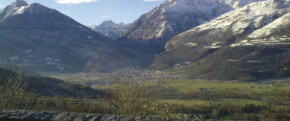 A mountainous landscape with snow-capped peaks, a valley with scattered buildings, and a stone wall in the foreground.