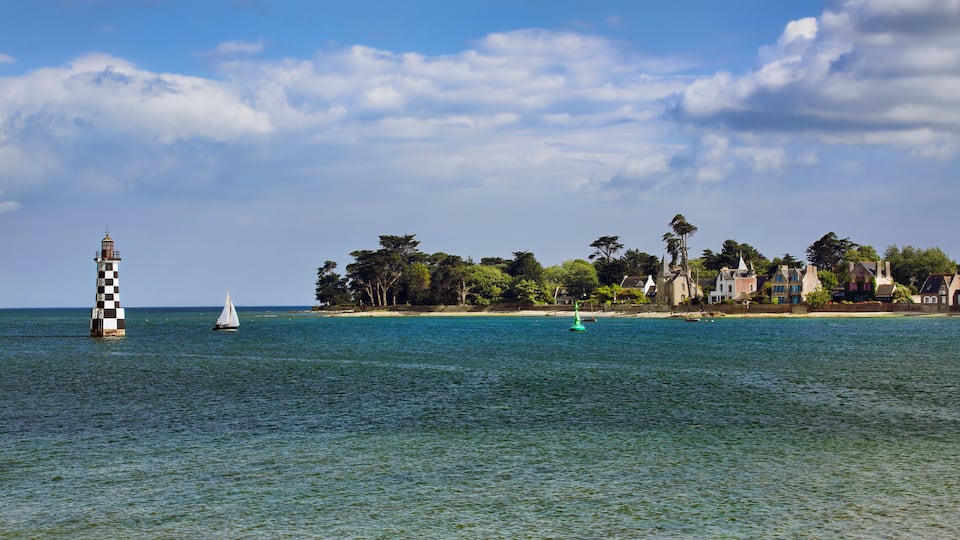 A lighthouse, sailboats, and a coastal town with historic houses.