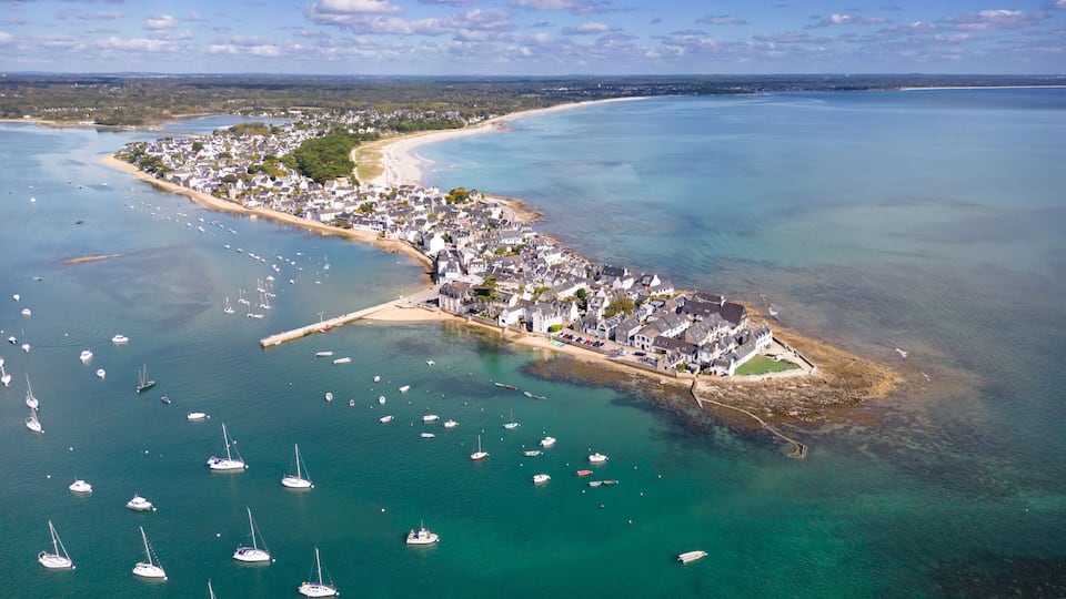 An aerial view of a coastal town with a marina, sandy beaches, and clear blue waters.