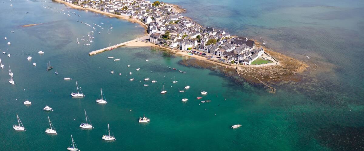 An aerial view of a coastal town with a marina, sandy beaches, and clear blue waters.