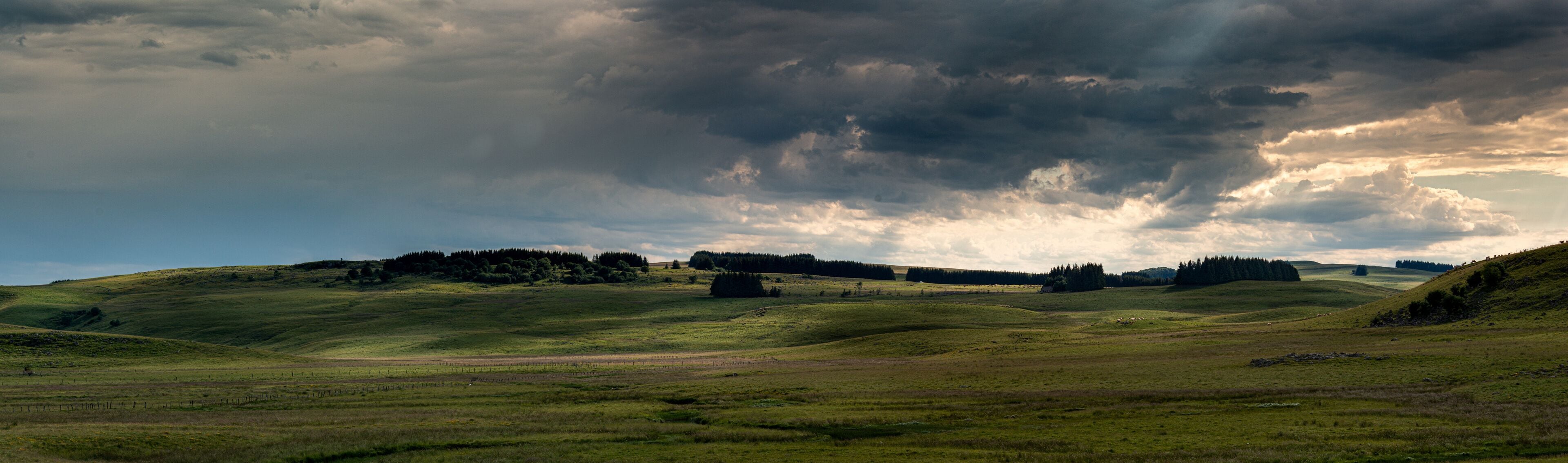 panorama of the Aubrac plateau in the evening with dramatic storm clouds & sun rays, rustic rural scene, Lozere France