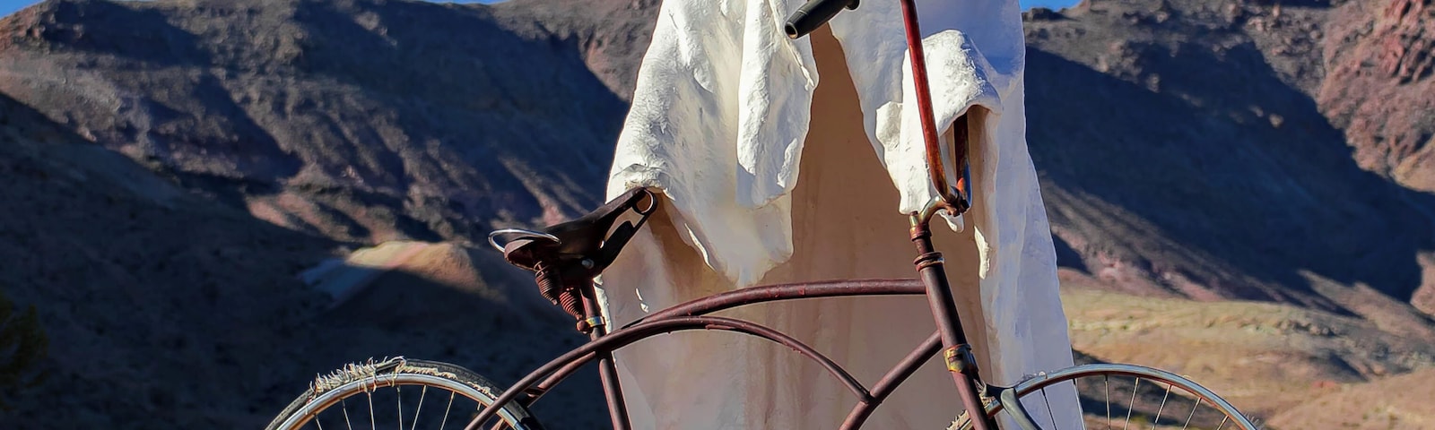 Una bicicleta con un paño blanco cubriéndola, con montañas al fondo.