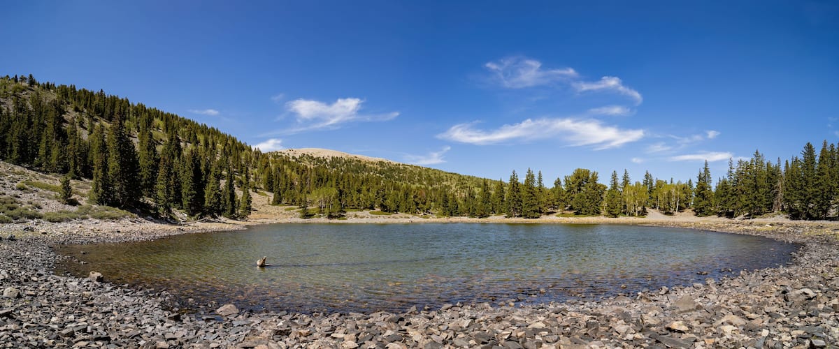 A clear lake surrounded by rocky terrain and dense forest.