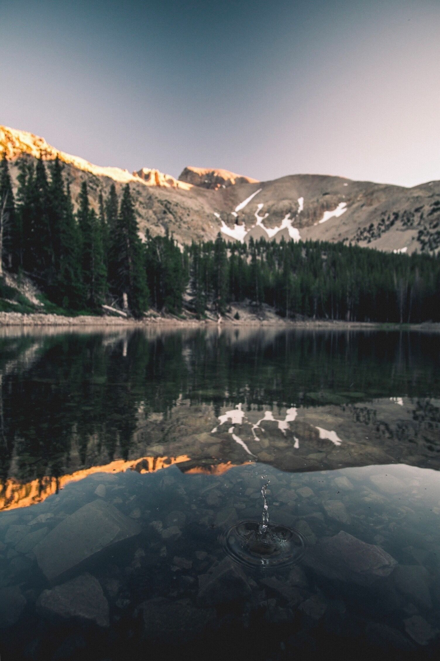A mountain lake with reflections of trees and mountains.