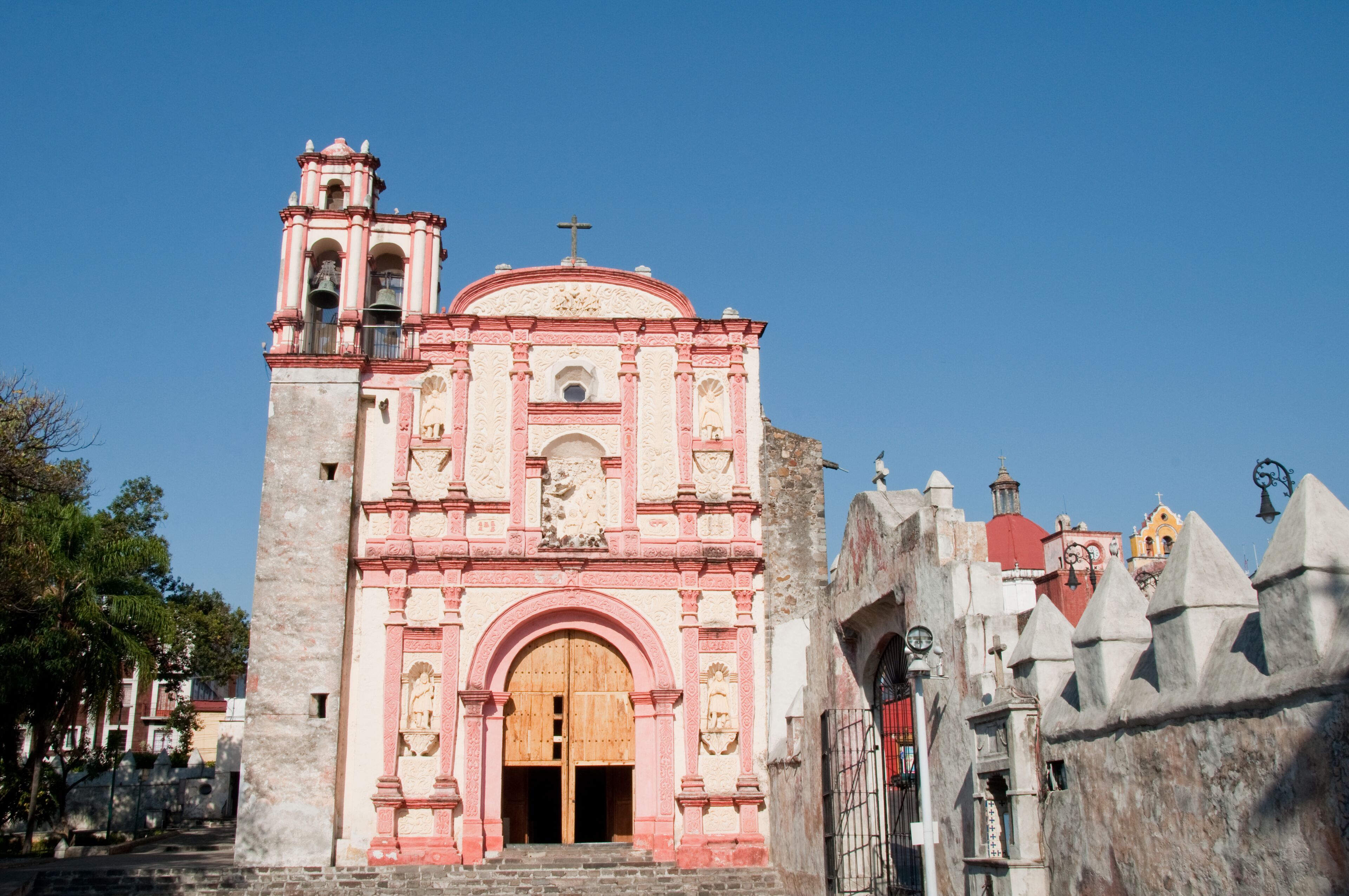 A pink and white church with a bell tower and a wooden door.