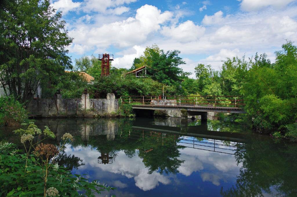 A tranquil river with a stone bridge, lush greenery, and a small tower.