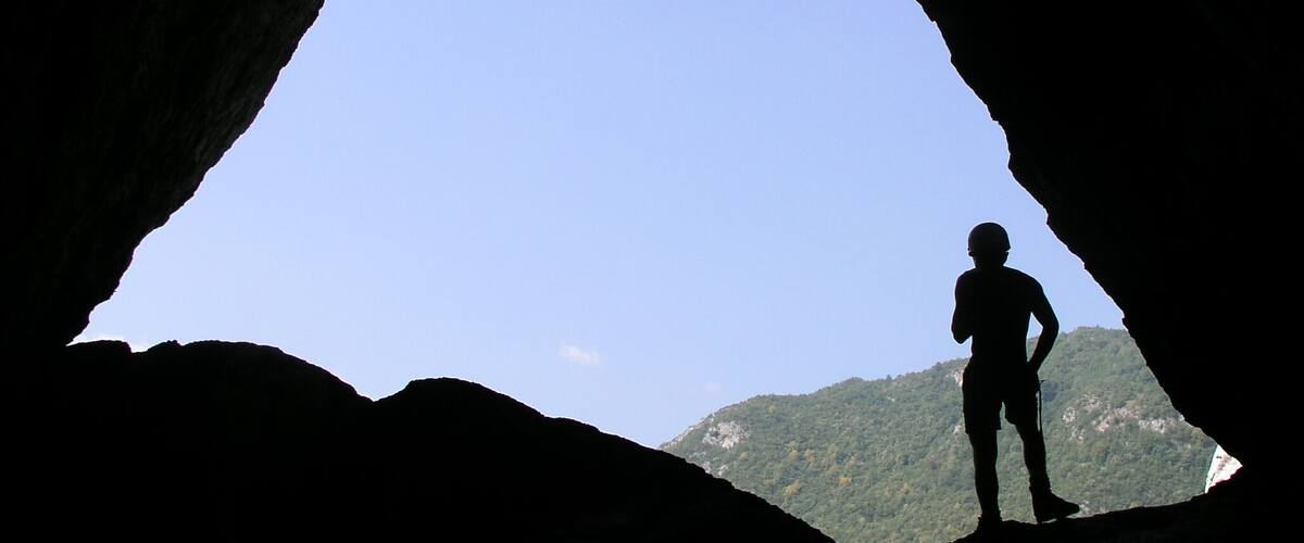 A person silhouetted against a clear sky, standing in a natural rock formation with a mountain in the background.