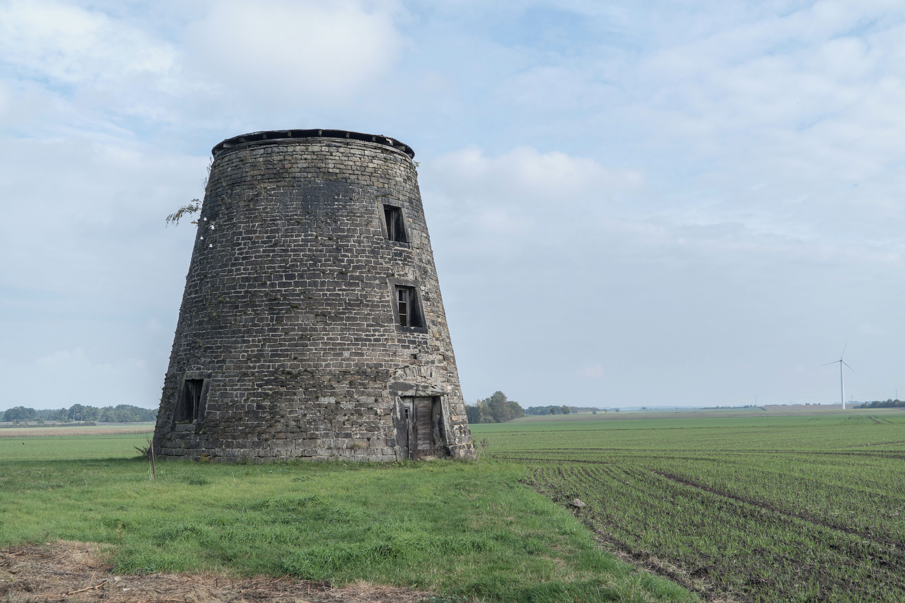 A stone tower in a field with wind turbines in the distance.