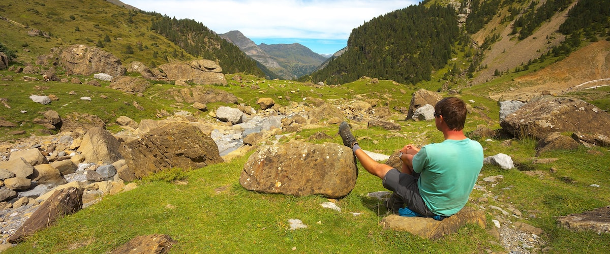 Resting tourist with one leg leaning against the stone in the mountain valley nearby resort of Gavarnie, Pyrenees