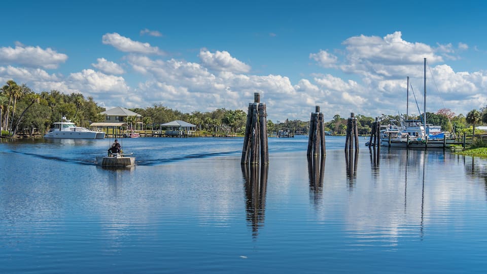 A calm lake with a boat, wooden posts, and a house in the background.
