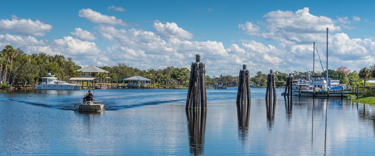 A calm lake with a boat, wooden posts, and a house in the background.