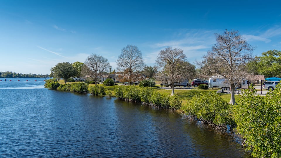 A calm lake with boats, a grassy area, trees, and RVs parked along the shore.