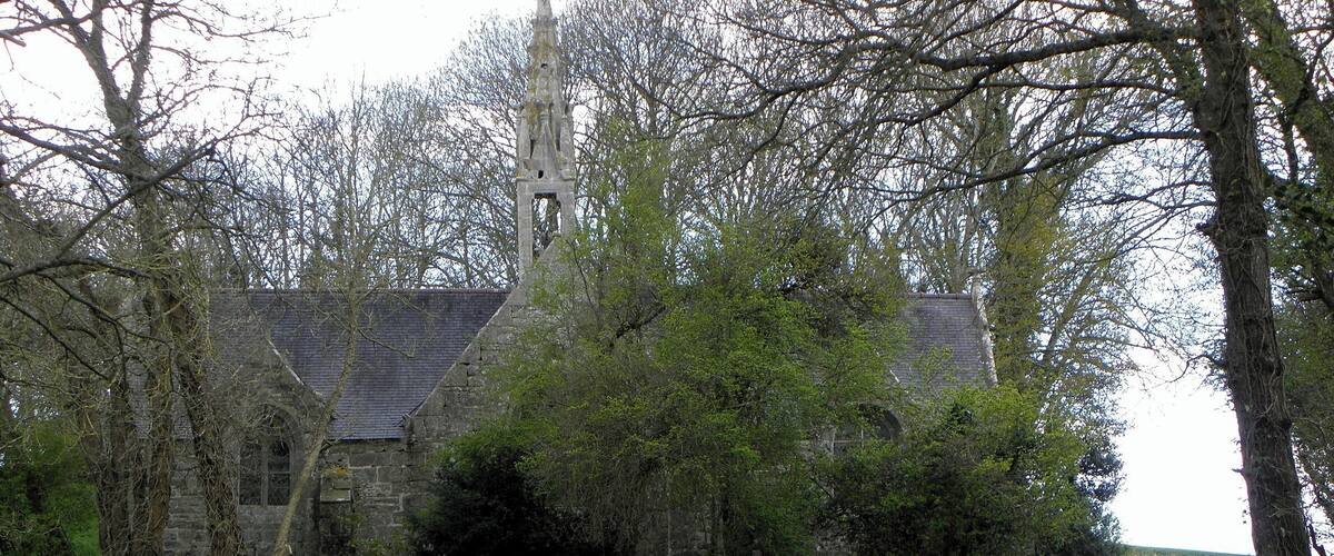 A stone church with a bell tower surrounded by trees and a gravel path.
