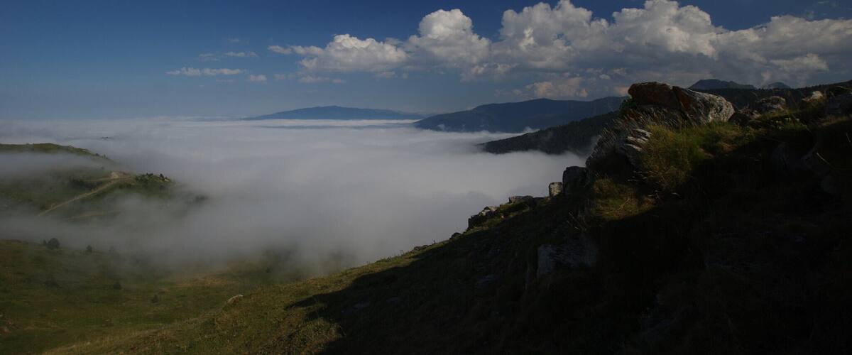 A mountainous landscape with a valley shrouded in mist, a clear blue sky, and scattered clouds.