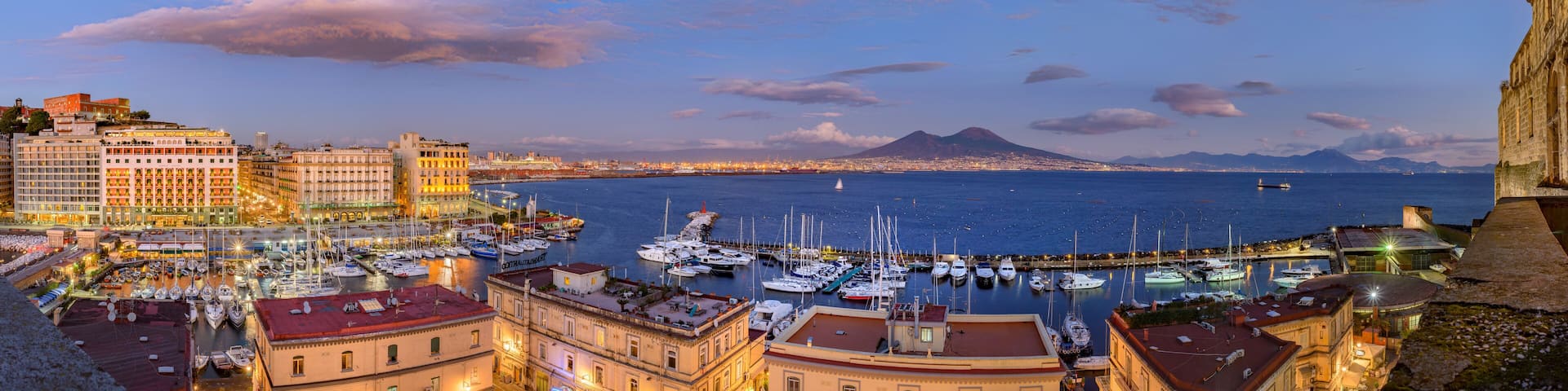 Naples, Italy. Splendid panoramic view from Castel dell'Ovo over the city and Borgo Marinari after sunset. Marina on Via Partenope with luxury hotels. Mount Vesuvius in the distance. 2012-12-19.