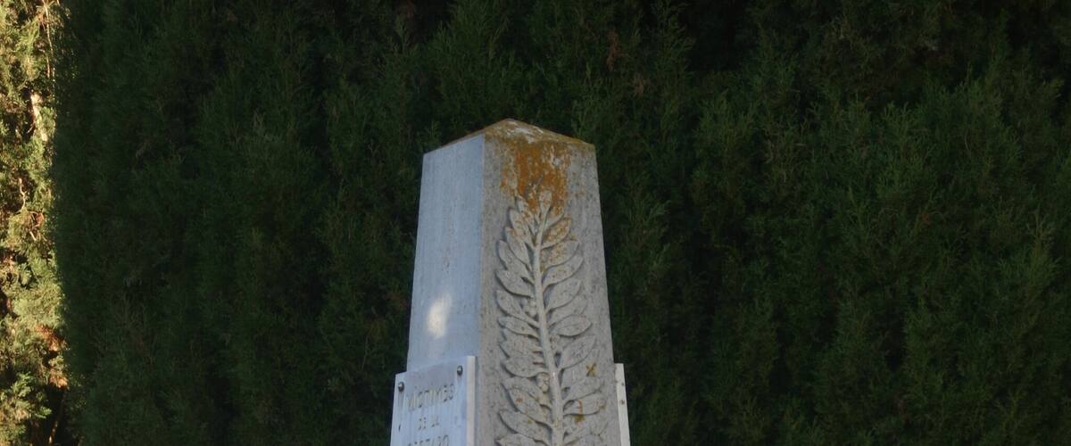 A gravestone with inscriptions and a cross, surrounded by a metal fence and flowers.