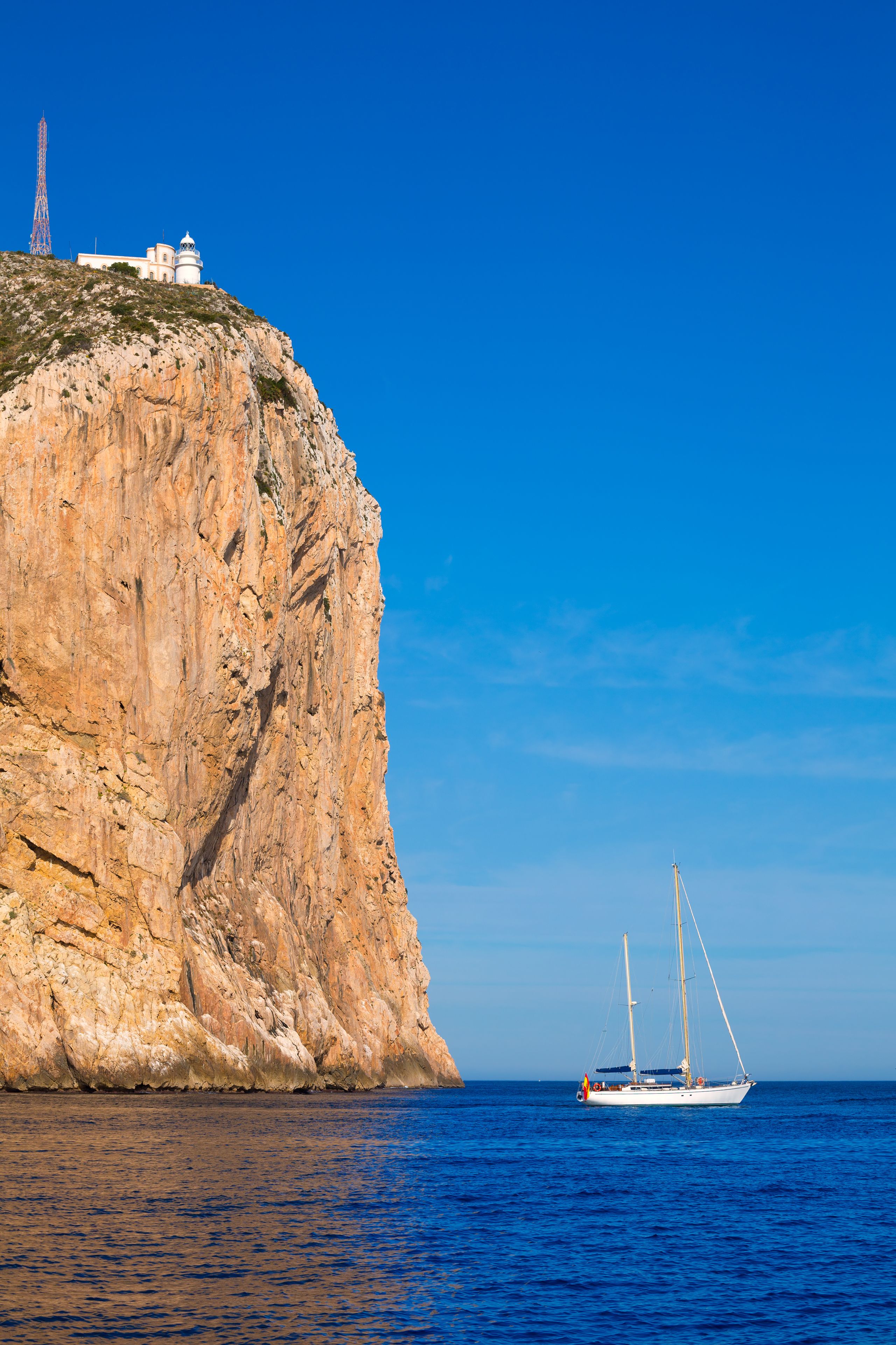 Una scogliera rocciosa con un faro e una barca a vela nell'acqua.