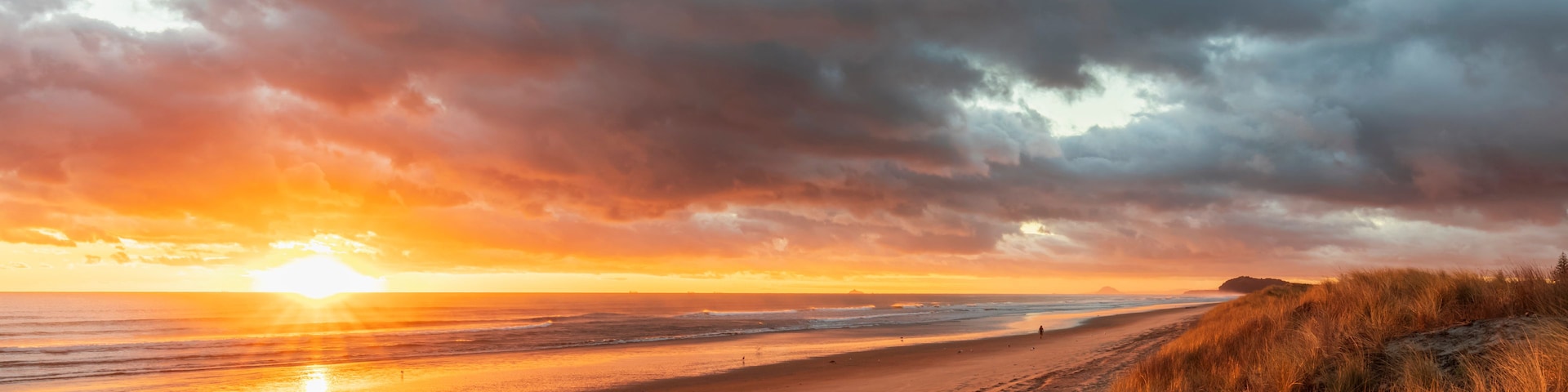 Uma praia com pôr do sol, ondas do oceano e dunas gramadas.