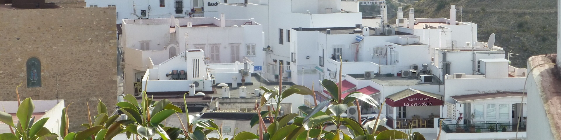 Um edifício branco com uma torre de relógio, rodeado por vegetação e montanhas.
