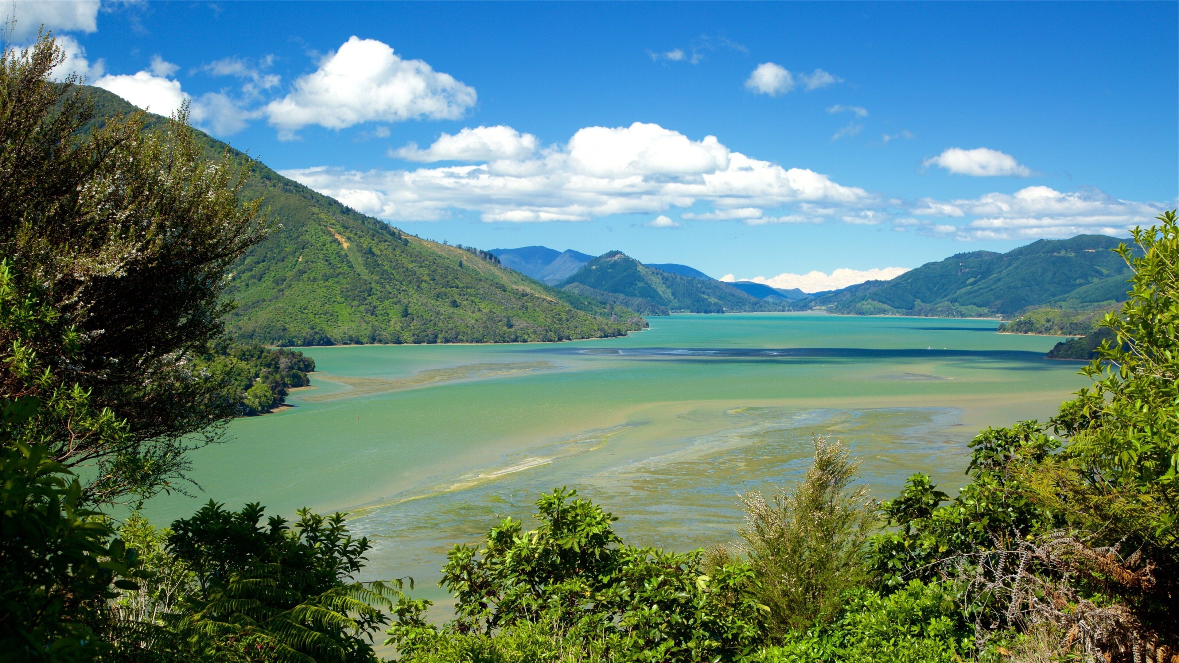 A coastal landscape with a bay, green hills, and a clear sky.