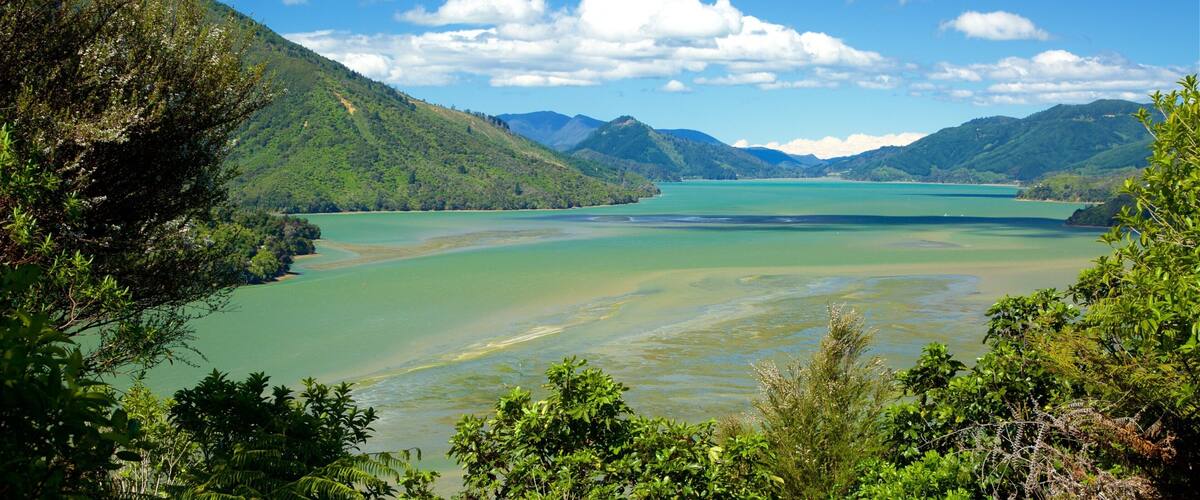 A coastal landscape with a bay, green hills, and a clear sky.