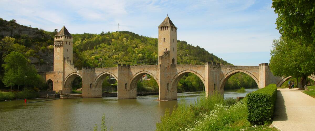 A stone bridge with towers over a river, surrounded by greenery and hills.
