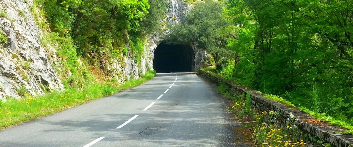 A road leading through a tunnel surrounded by lush greenery and rocky cliffs.