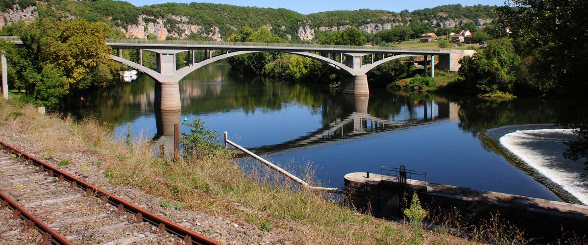A bridge over a calm river with surrounding greenery and hills.