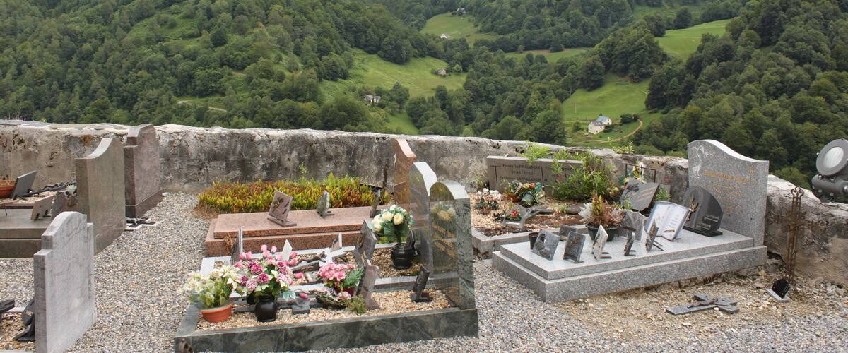 A cemetery with gravestones and flowers, surrounded by lush green hills and a cloudy sky.
