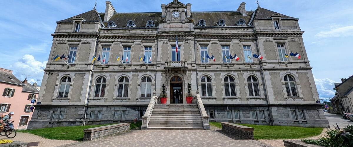 A large, historic building with a grand entrance, multiple flags, and a clock tower.