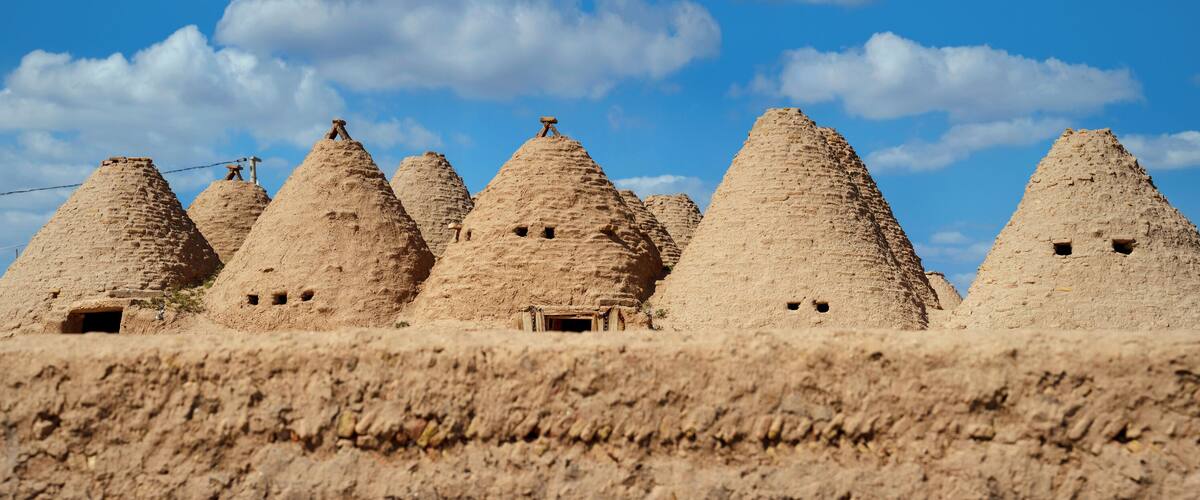 A series of conical mud-brick structures with small openings, set against a clear blue sky.