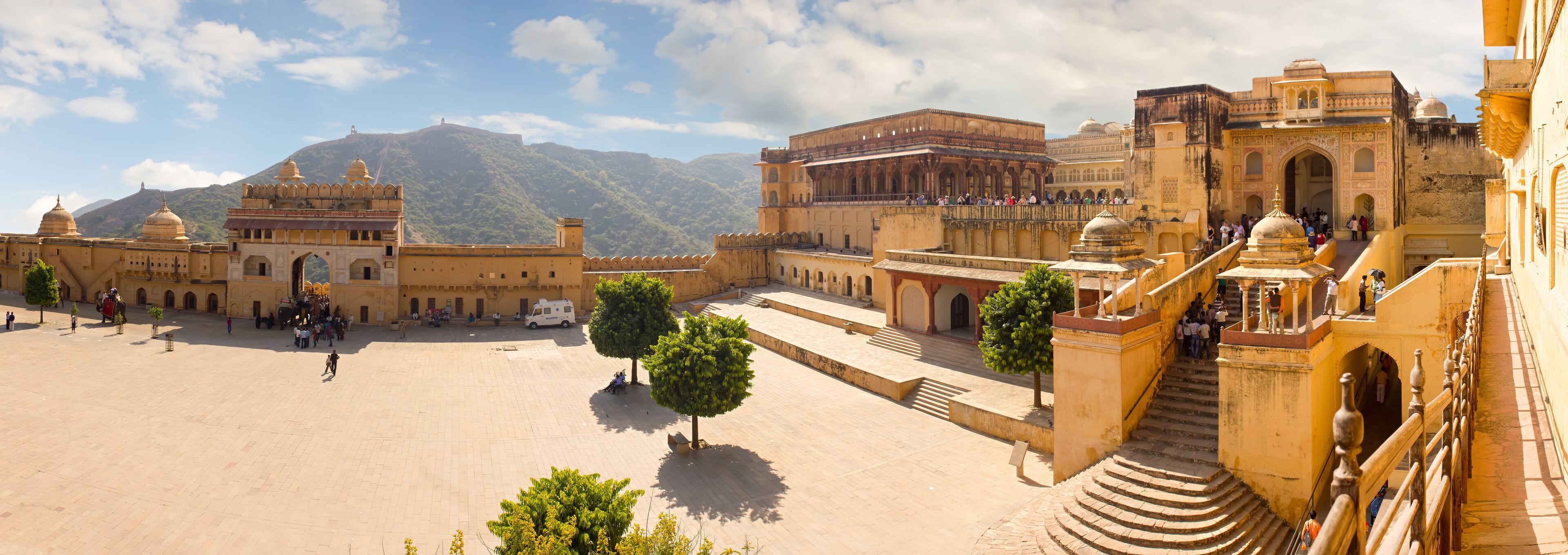 A historic palace complex with large courtyards, domed structures, and a mountainous backdrop.