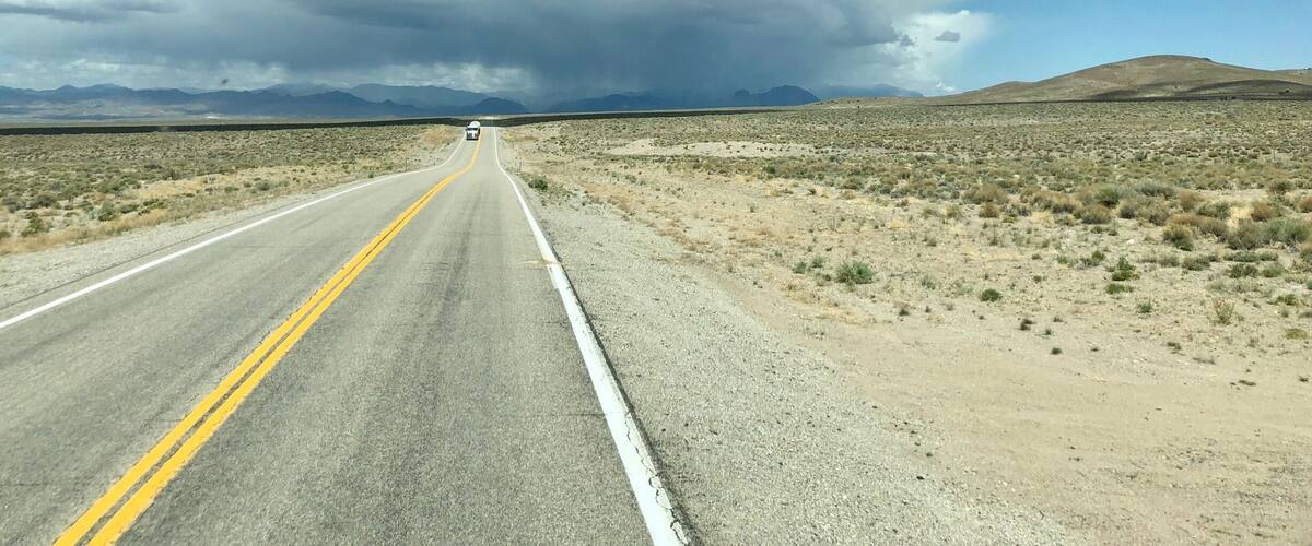 A road in a desert landscape with mountains in the distance and a stormy sky.