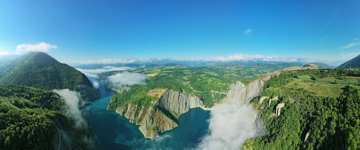 A mountainous landscape with a river, lush greenery, and distant snow-capped peaks.