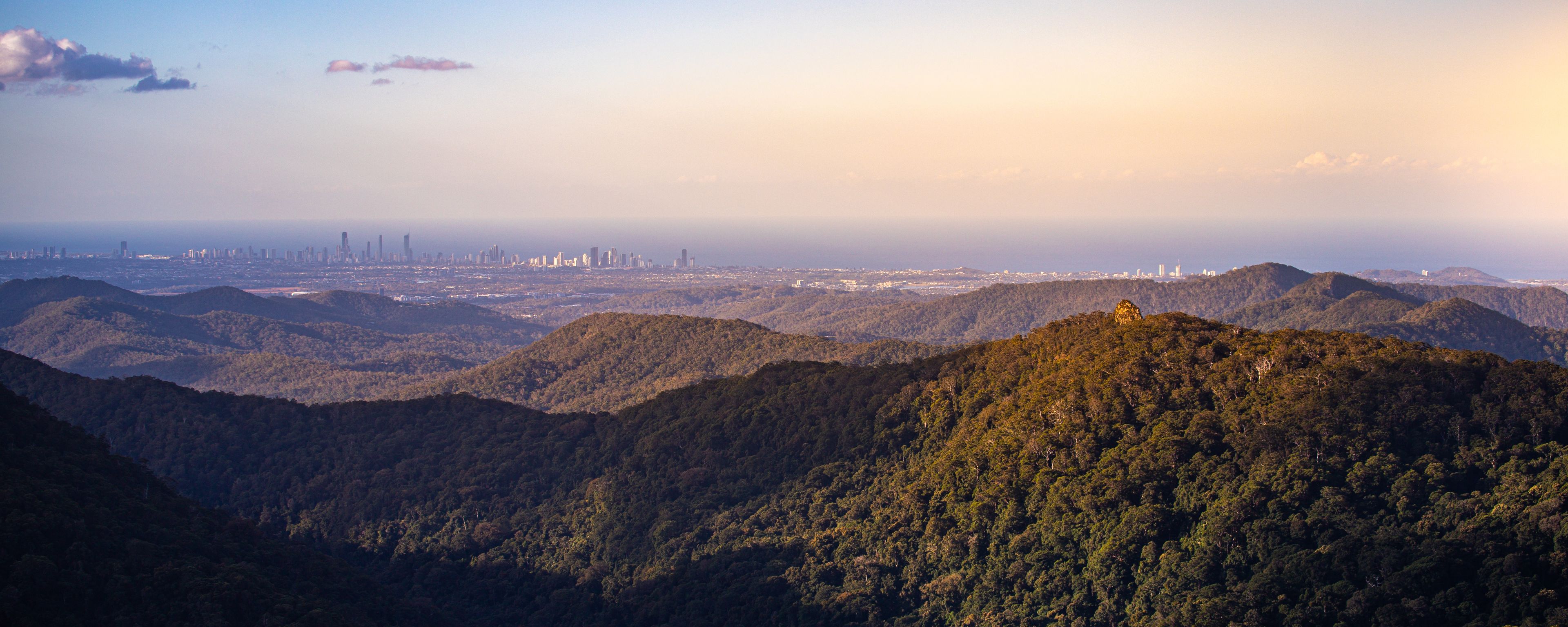 Un paysage montagneux, avec de vastes forêts et, au loin, les contours d’une ville.