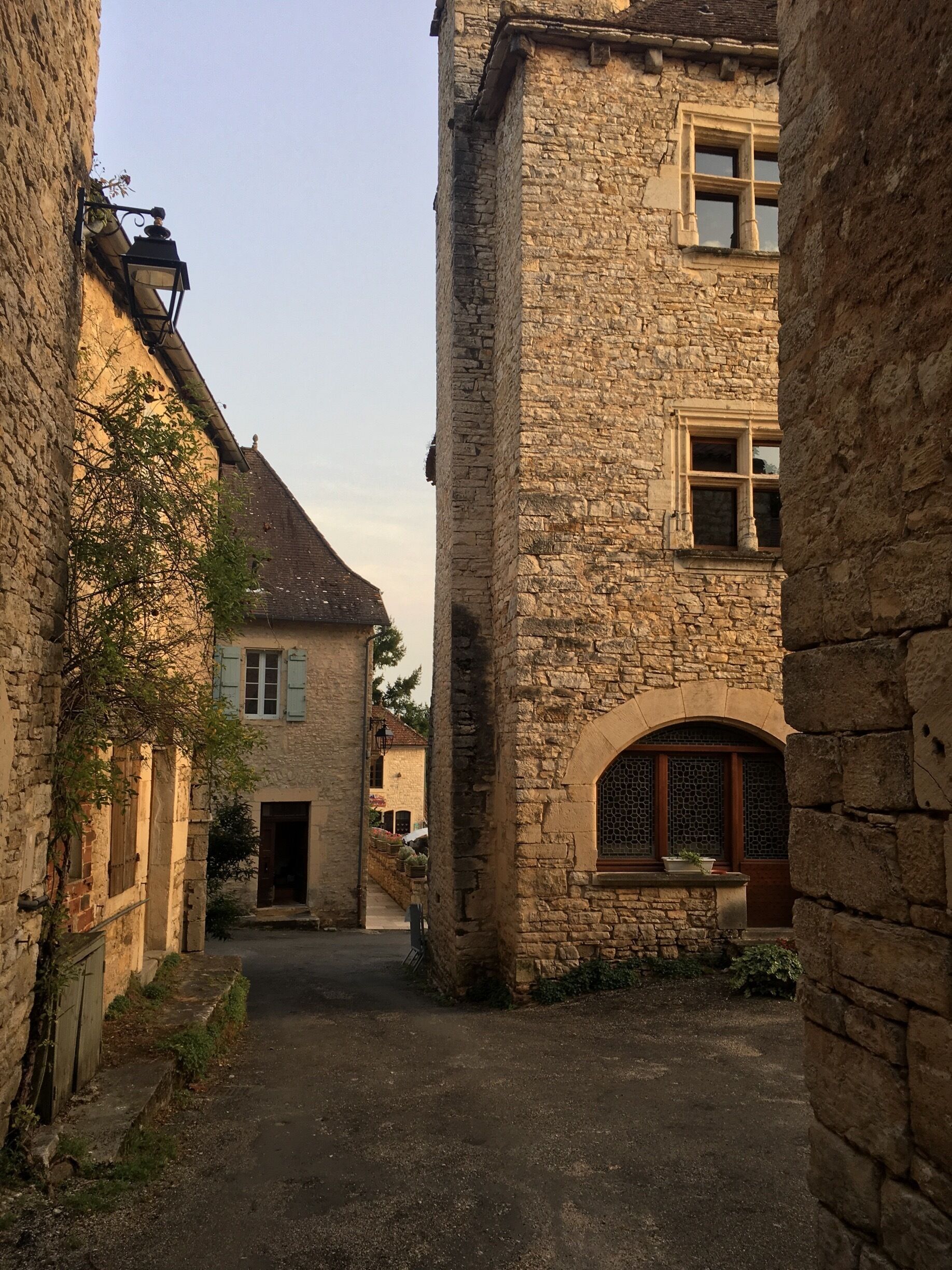 A narrow cobblestone street flanked by historic stone buildings with arched windows and shutters.