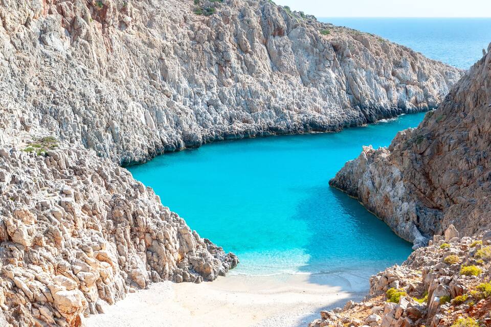 Una costa rocciosa con una baia turchese e una spiaggia di sabbia.