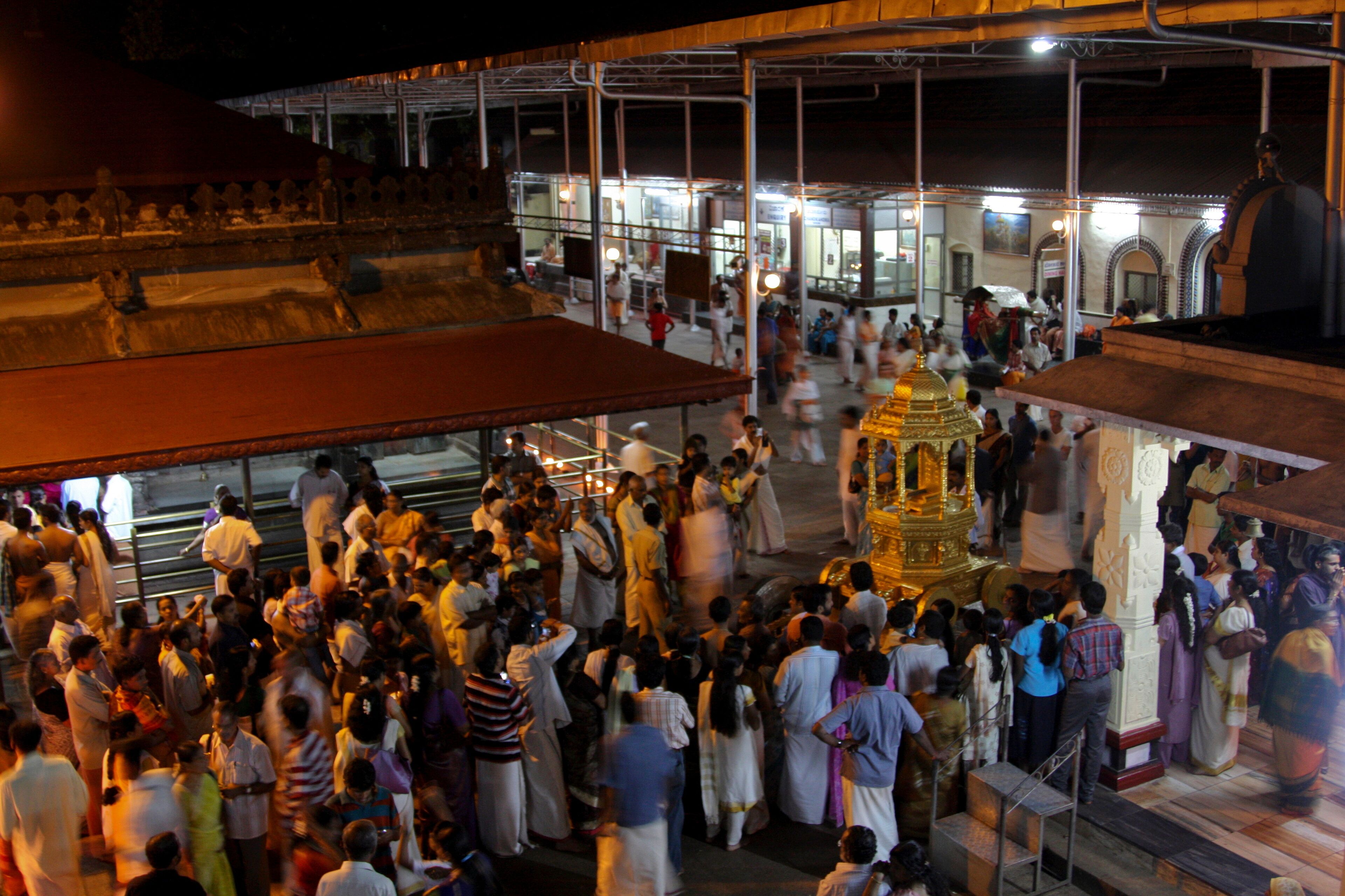 A crowded temple with a golden statue and people in traditional attire.