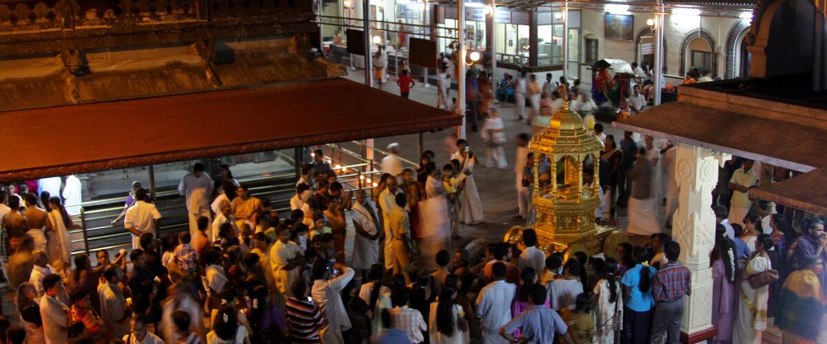 A crowded temple with a golden statue and people in traditional attire.