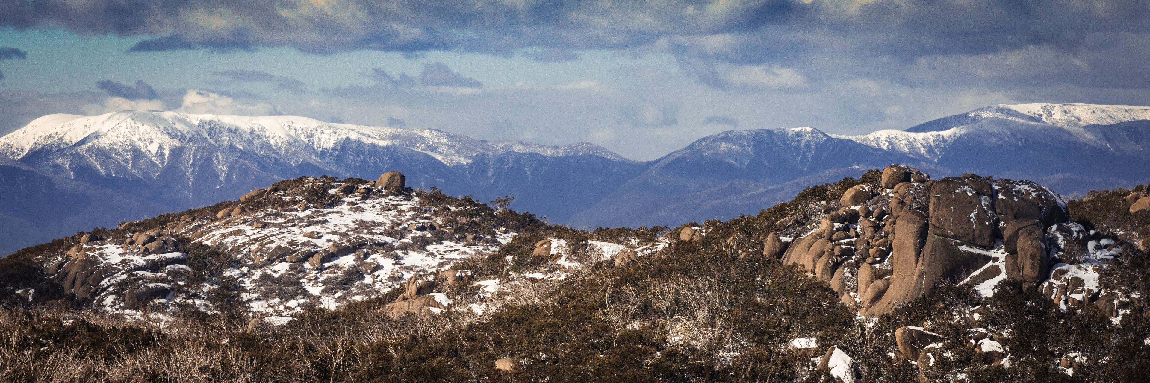 A snow-covered mountain range with rocky outcrops and sparse vegetation.