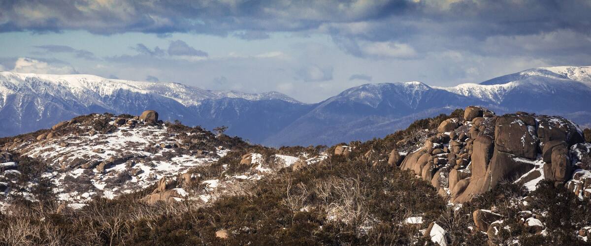 A snow-covered mountain range with rocky outcrops and sparse vegetation.