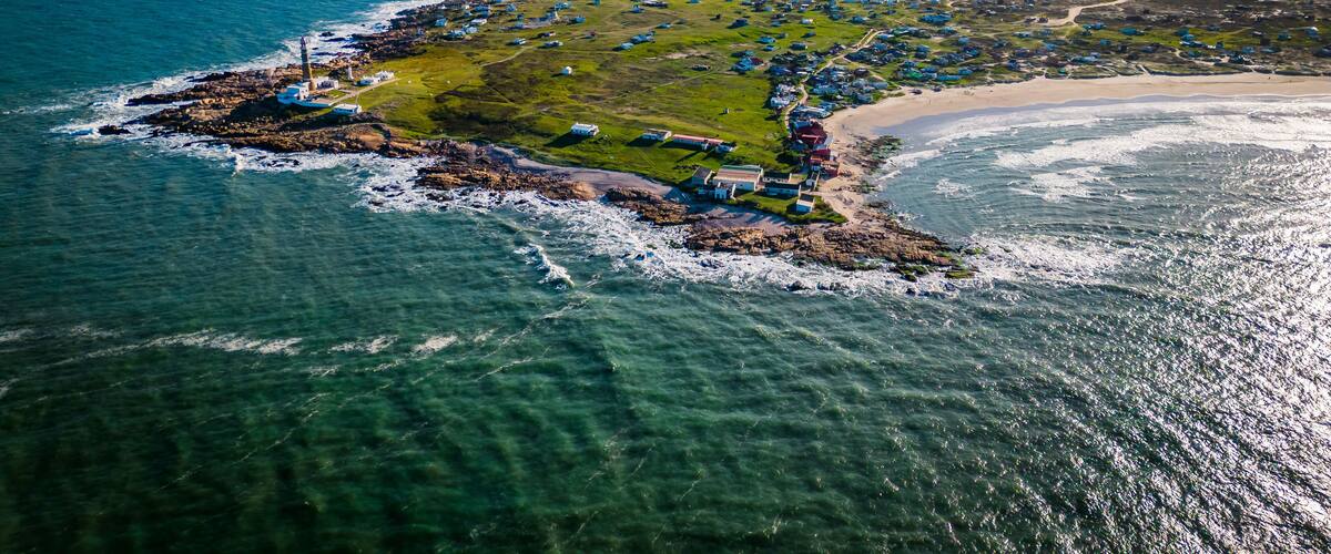An aerial view of a coastal village with houses, a lighthouse, and a beach.