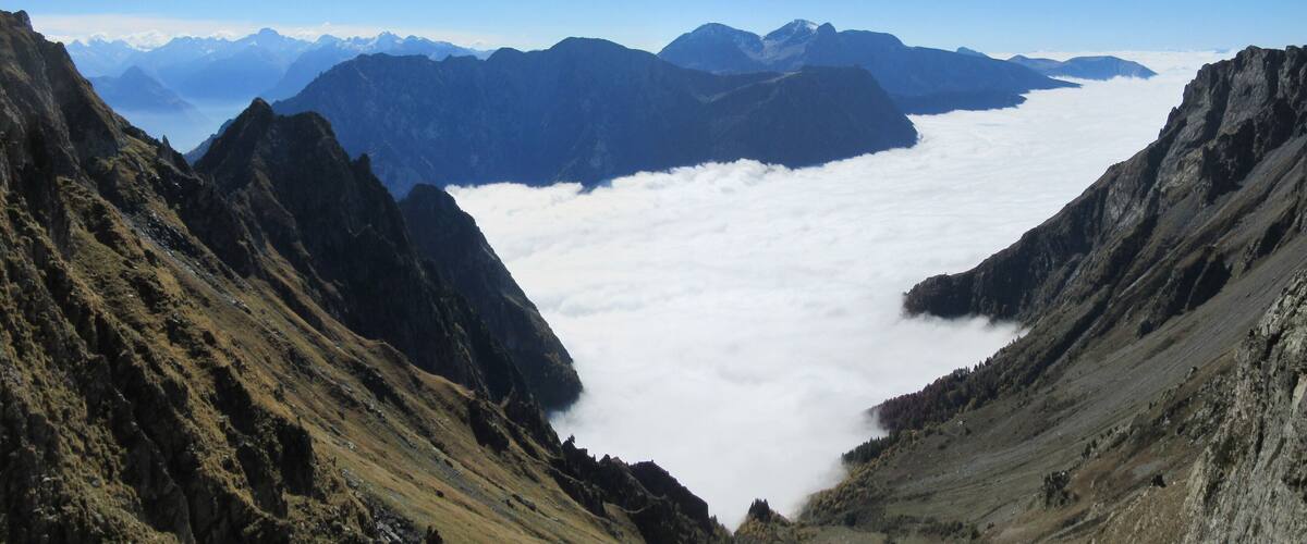 A mountain landscape with a valley and a cloud-covered mountain range in the background.