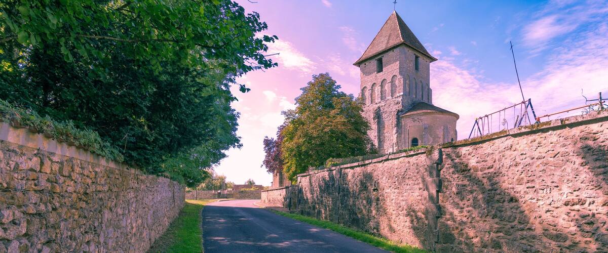 A narrow road flanked by stone walls, leading to a historic tower with a conical roof.