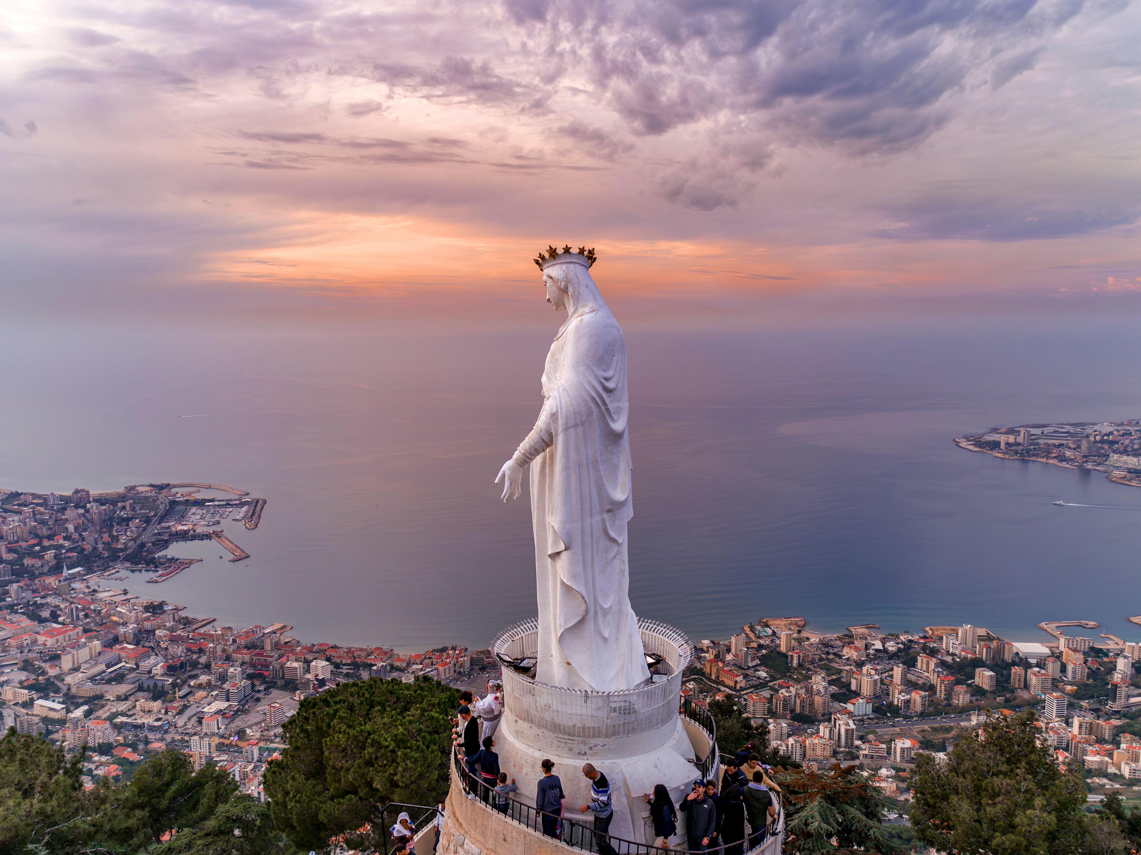 Una estatua con vistas a una ciudad costera al atardecer.