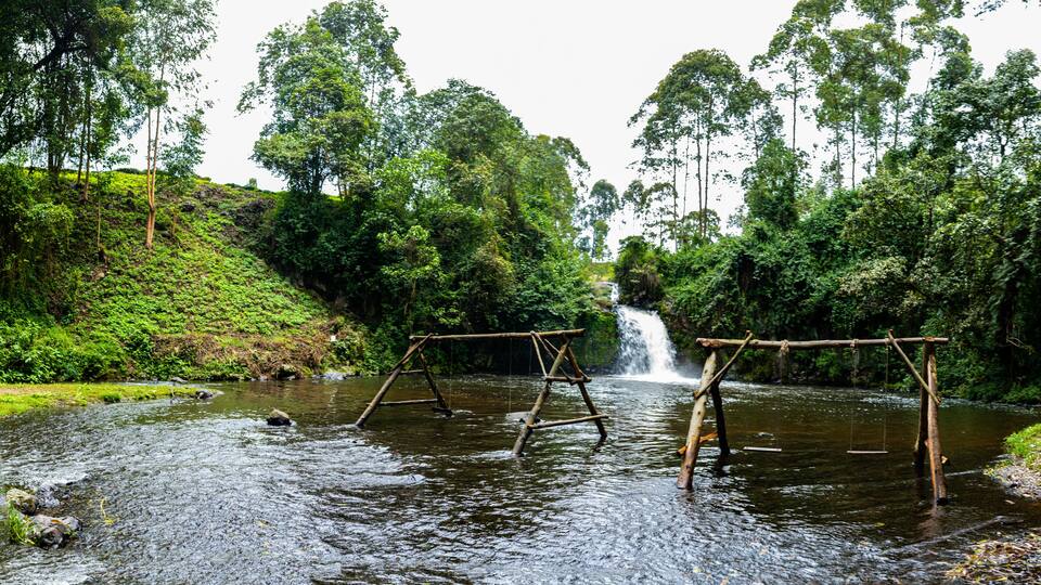 A river with wooden swings and a waterfall in a forested area.