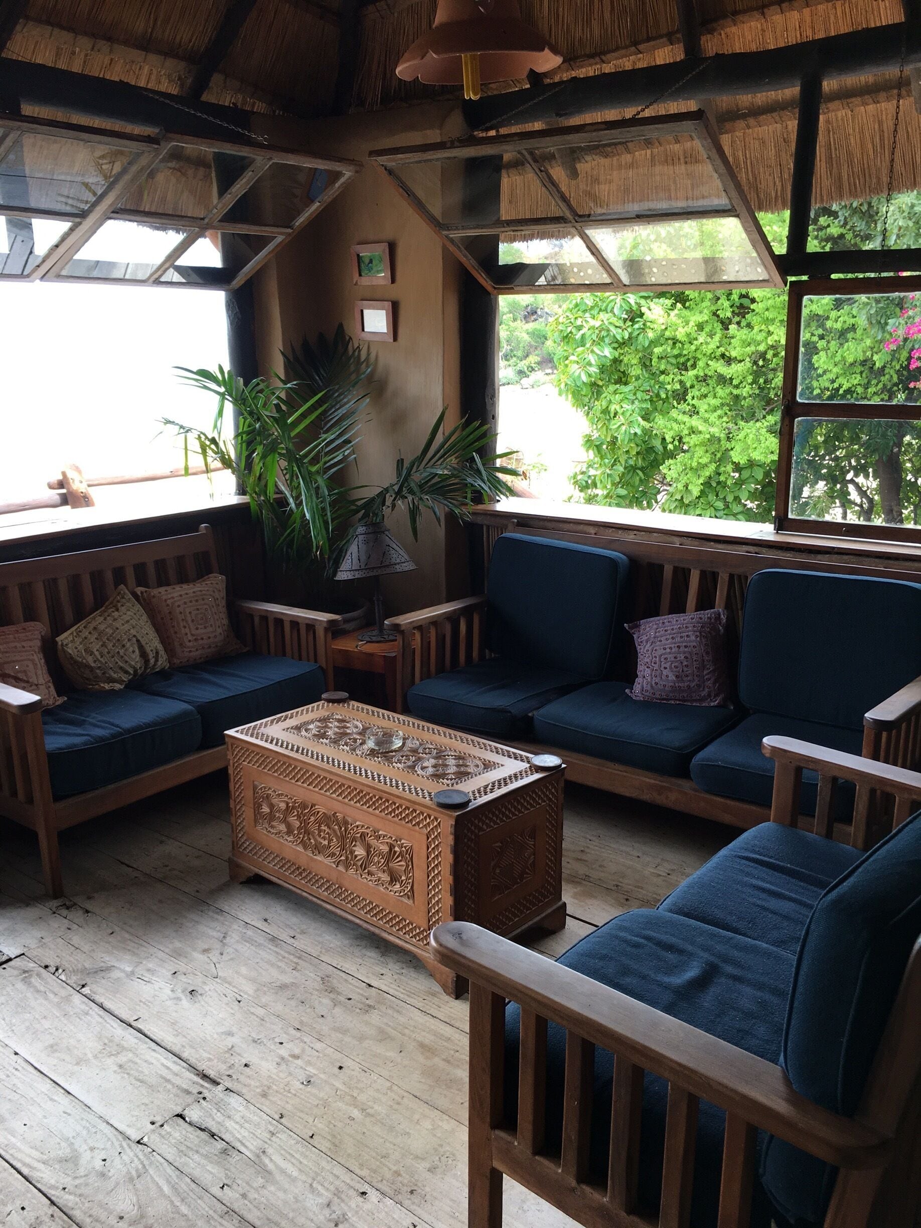 Un espacio interior acogedor con muebles de madera, una mesa de centro tejida y ventanas amplias con vistas a follaje.