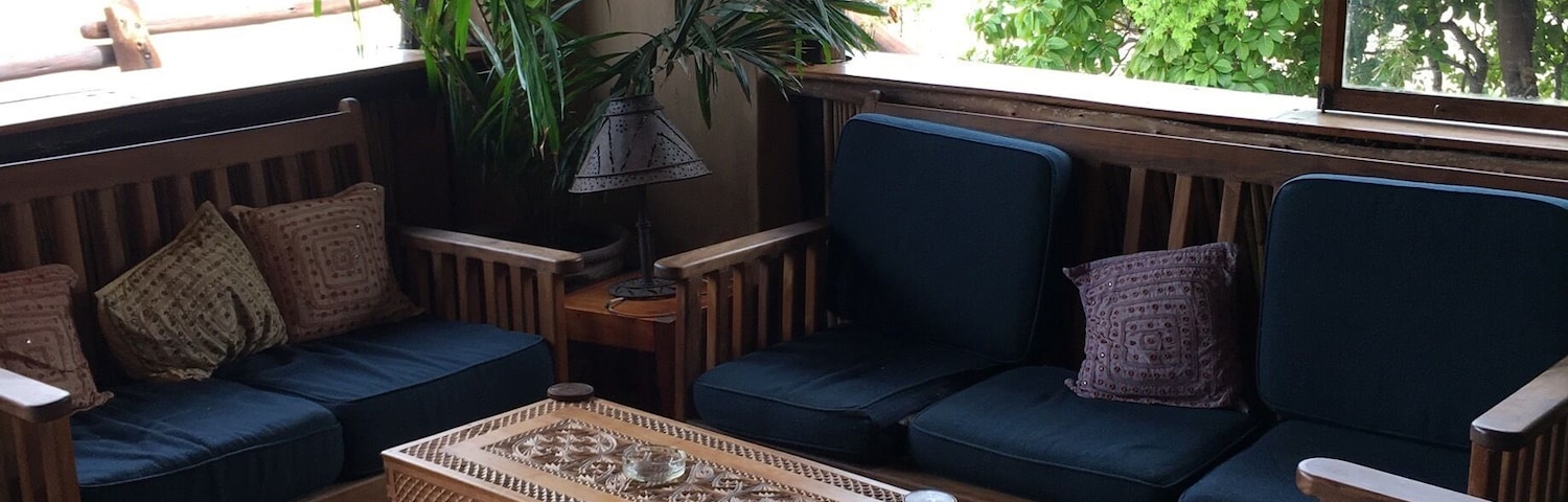 Un espacio interior acogedor con muebles de madera, una mesa de centro tejida y ventanas amplias con vistas a follaje.