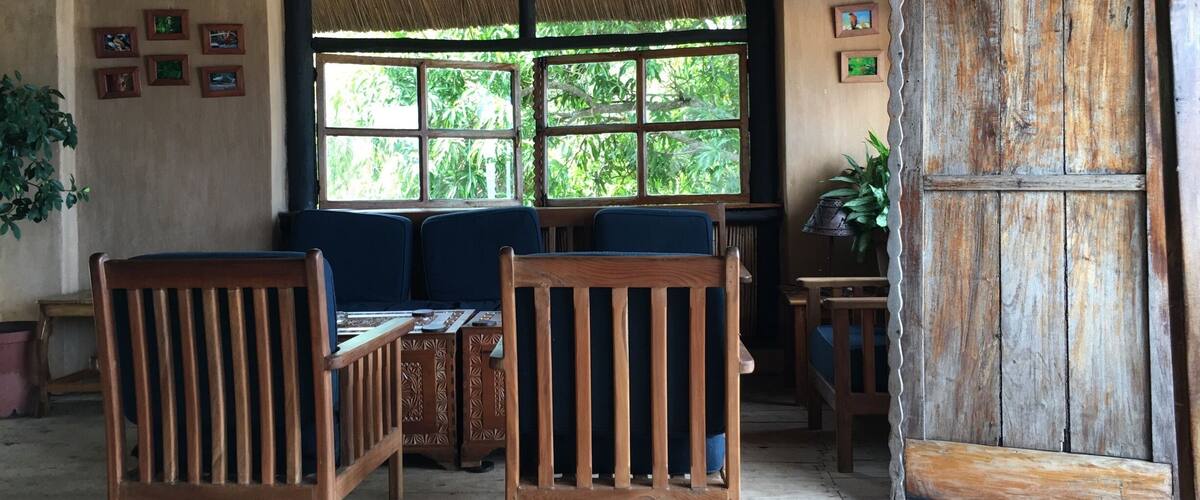 A rustic interior with wooden furniture, a thatched roof, and a large window overlooking greenery.