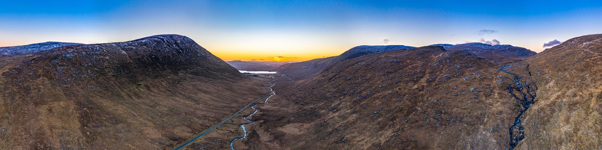 Un valle con un río serpenteante y colinas nevadas bajo un cielo al atardecer.
